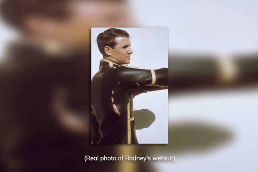 Color photo of a man wearing a custom black wetsuit with yellow vertical stripes, shown from the side with his arm extended. The caption below the image reads “(Real photo of Rodney’s wetsuit),” indicating this is a historical or documentary reference.
