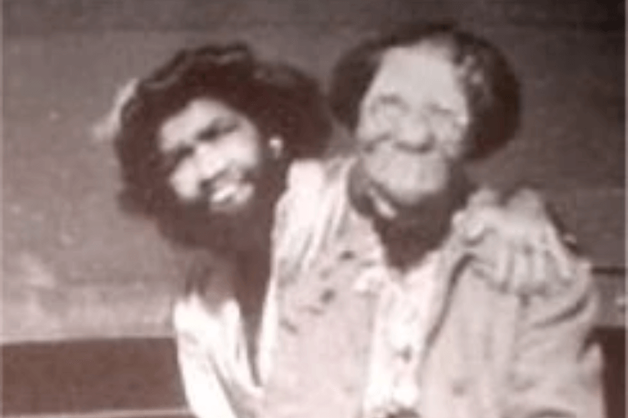 Grainy black and white photograph of two women with rare physical conditions seated side by side, one with hypertrichosis (excessive facial hair, often referred to historically as the "bearded lady") and the other with significant facial deformities. They are smiling and embracing, conveying warmth, solidarity, and shared experience despite the exploitative environments many such individuals were placed in during the sideshow era.