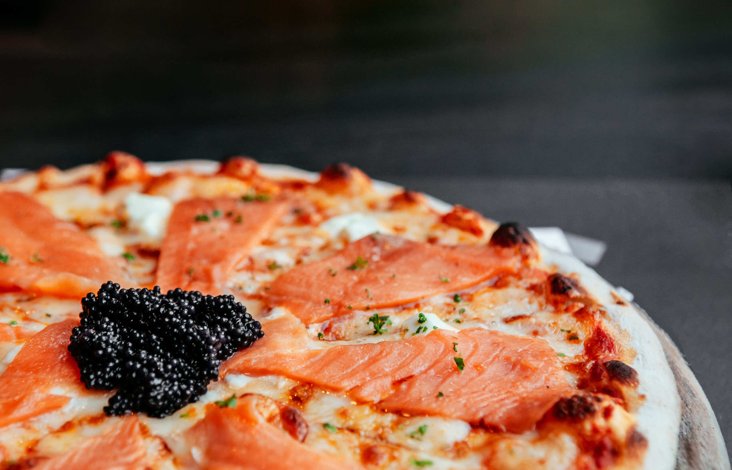 Delicious smoked Salmon thin crispy italian pizza with premium black Caviar close up shot