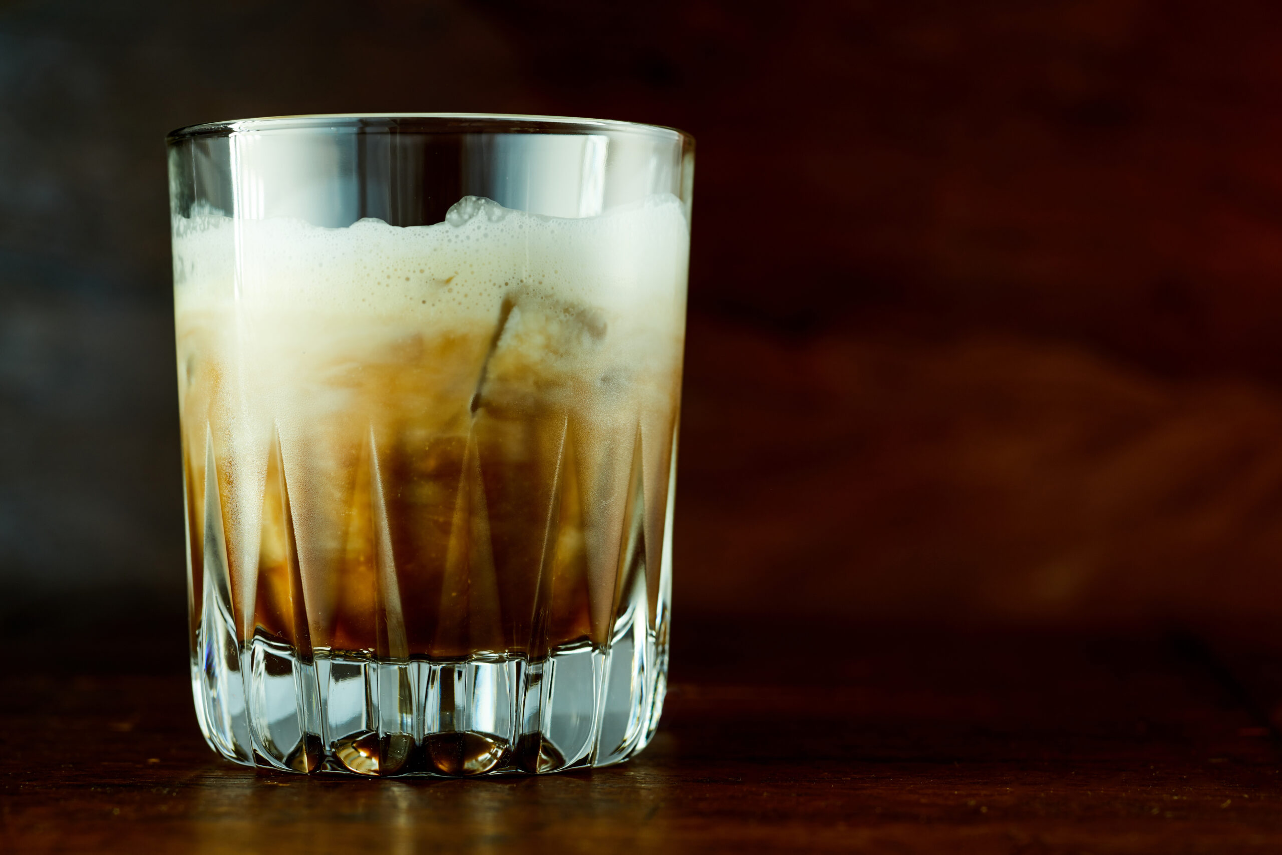 Delicious White Russian cocktail with vodka and coffee liqueur served with ice in old fashioned glass against dark background