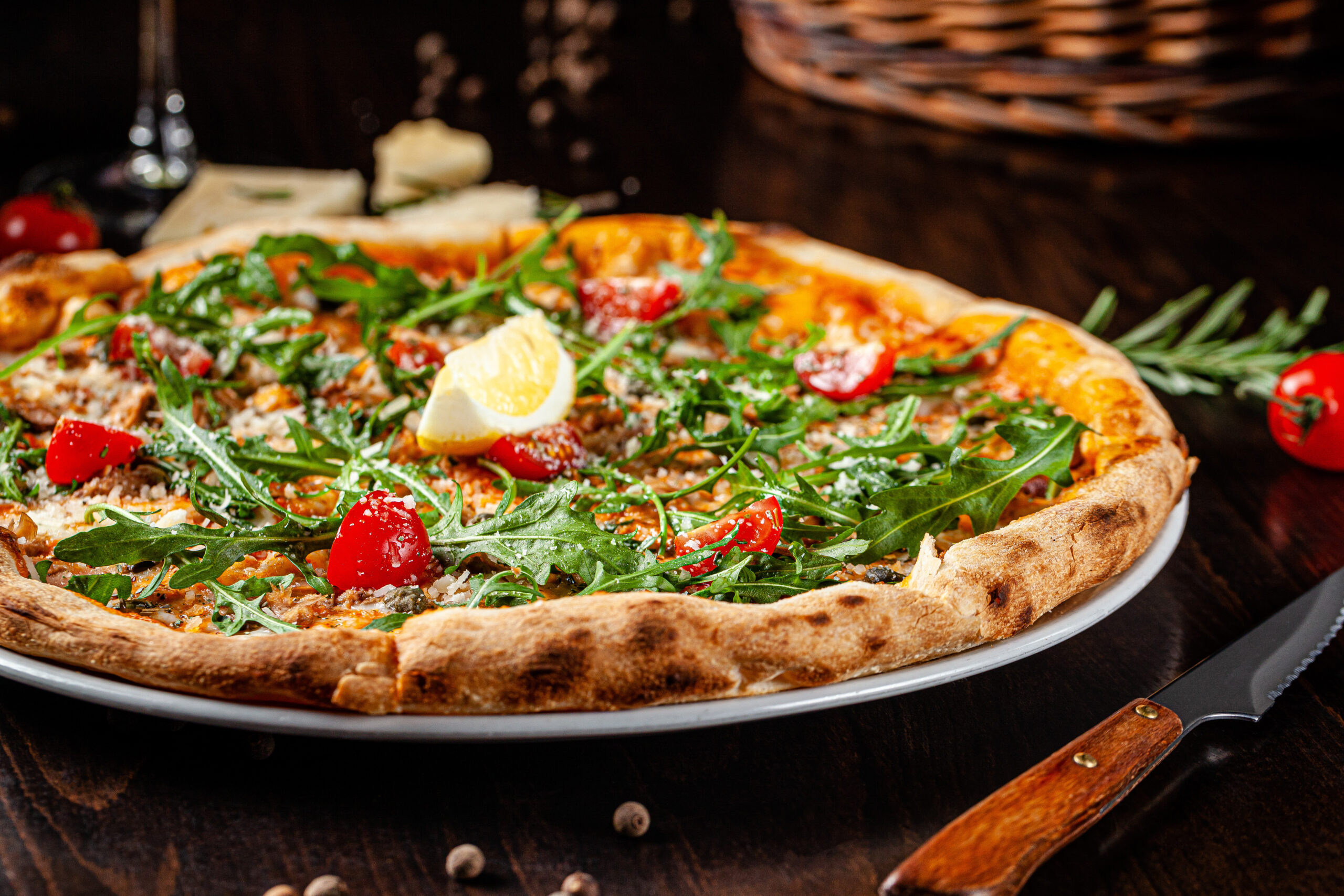 Italian Cuisine. Thin pizza with thick sides. Pizza in tomato sauce with capers, arugula, Parmesan cheese, cherry tomatoes and cod fish liver. background image, copy space text