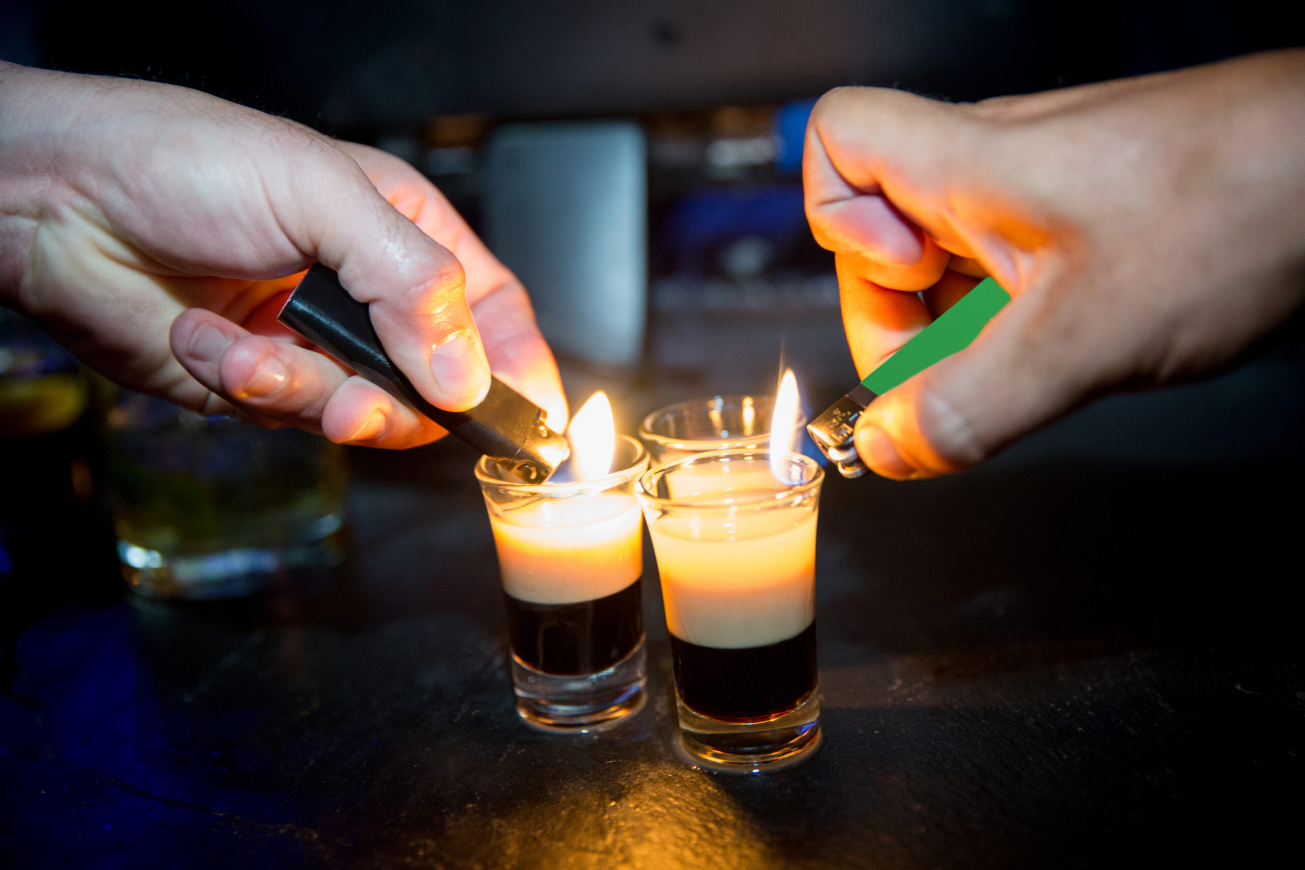 Bartender lit up fire on b52 shot drinks. Close up man hands holding lighter and lit up fire on alcoholic drinks, on shot glass of b52, consist of kahlua on shots. The man hands are on top of the bar.