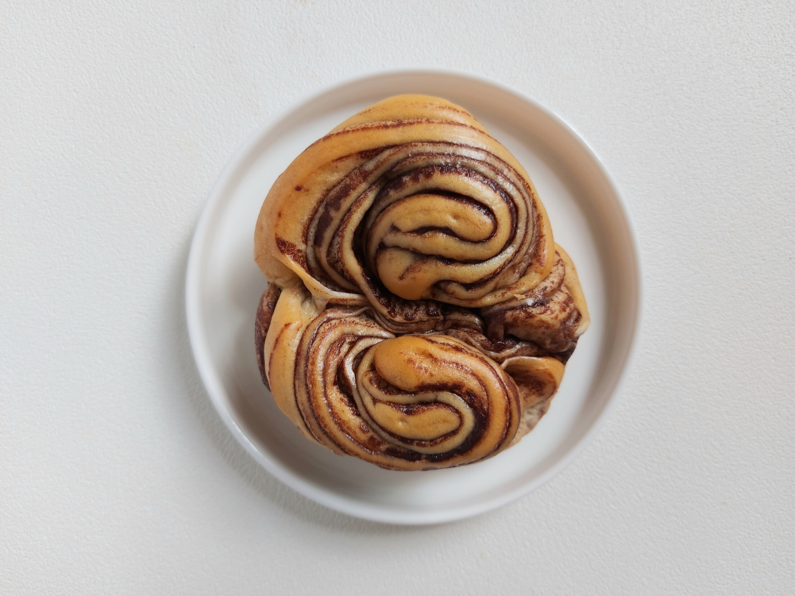 Chocolate swirl bun on white plate. Soft and sweer taste. Minimalist and aesthetic photography concept. Top view or flat lay. Isolated background in white