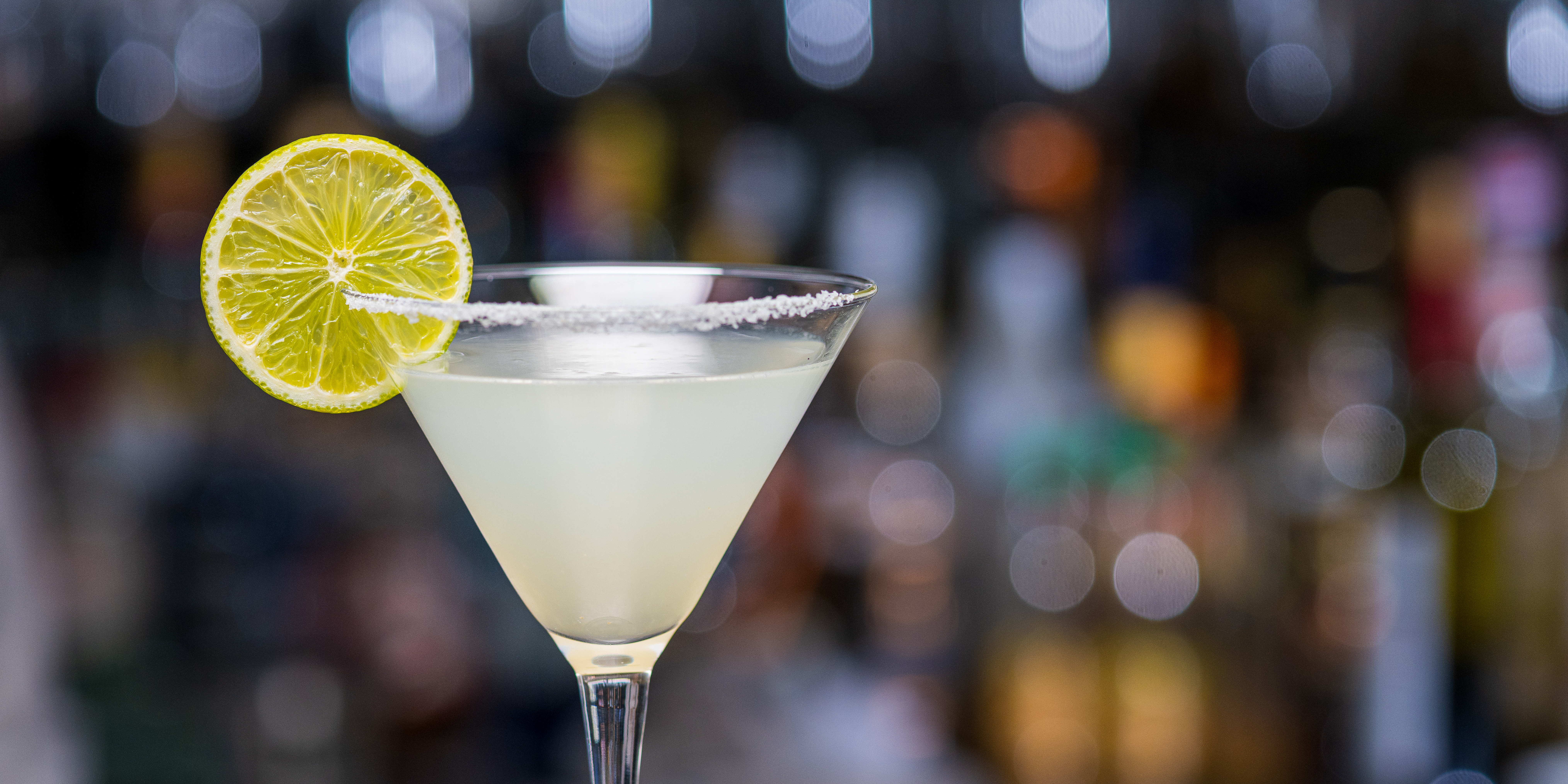 Close-up of martini cocktail with lemon slice in bar.