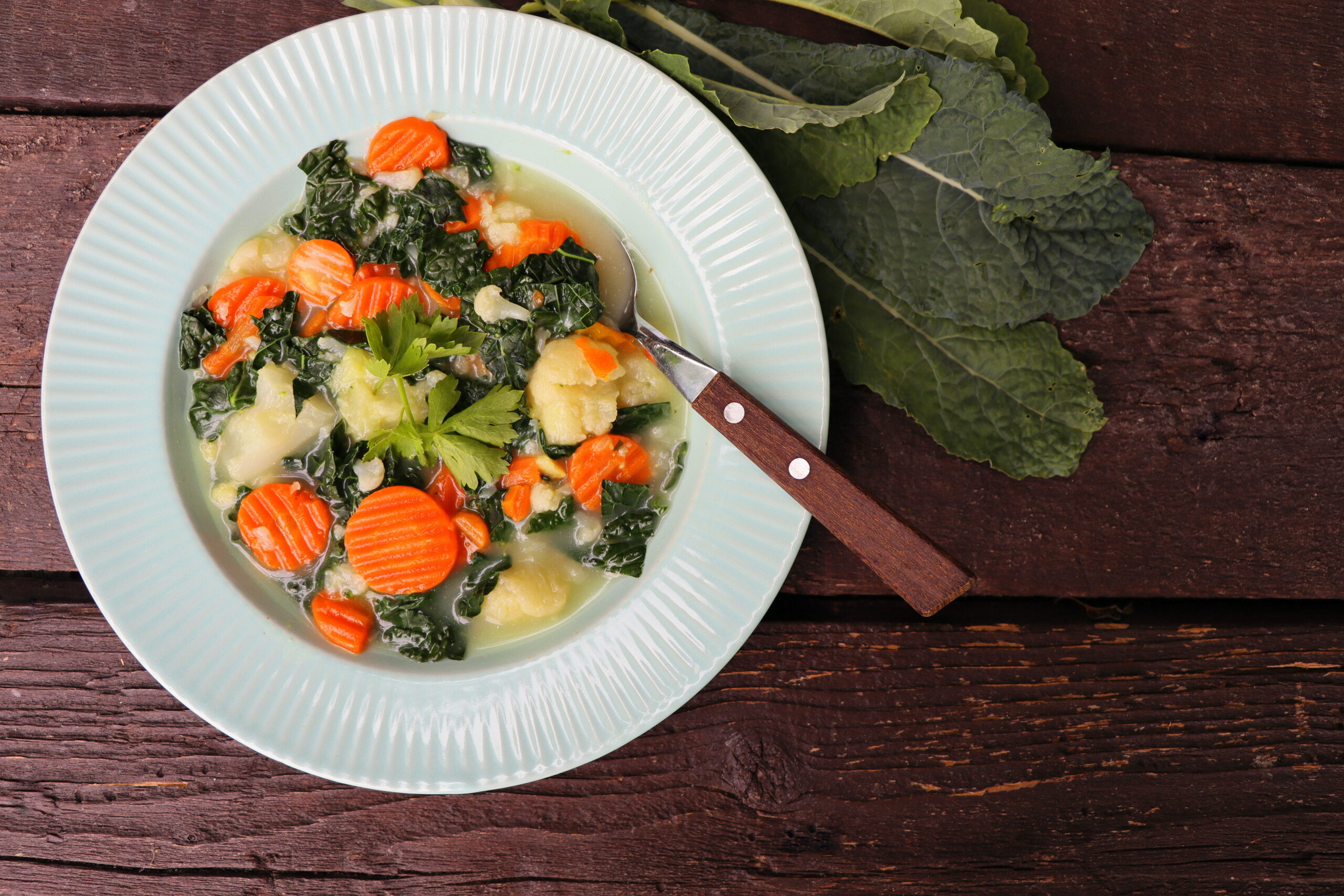 Healthy vegetable soup with kale. Above view table scene on a dark wood background .