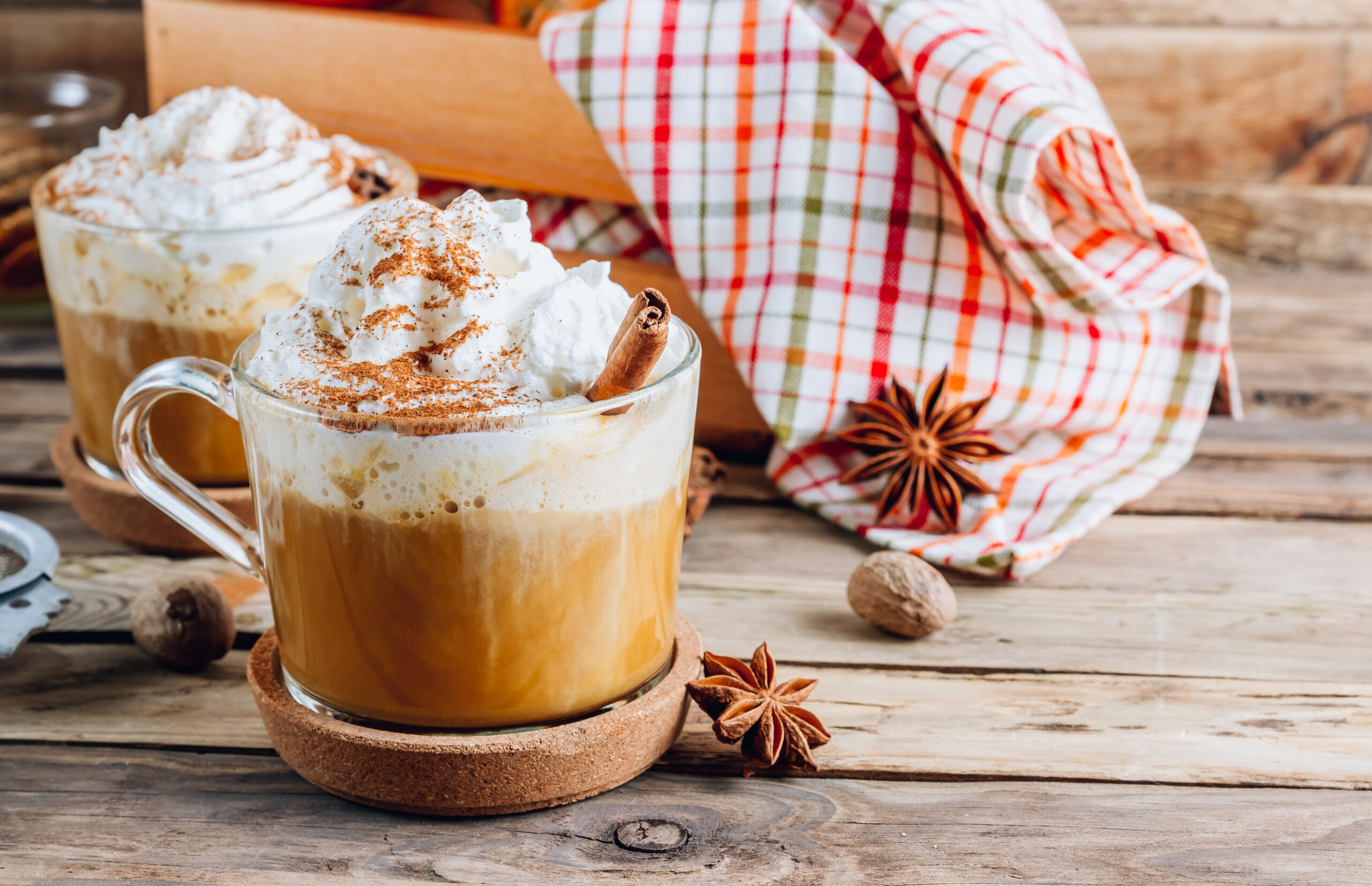 Pumpkin spiced latte in a glass mug on a vintage wooden background. Autumn or winter hot drink. Selective focus