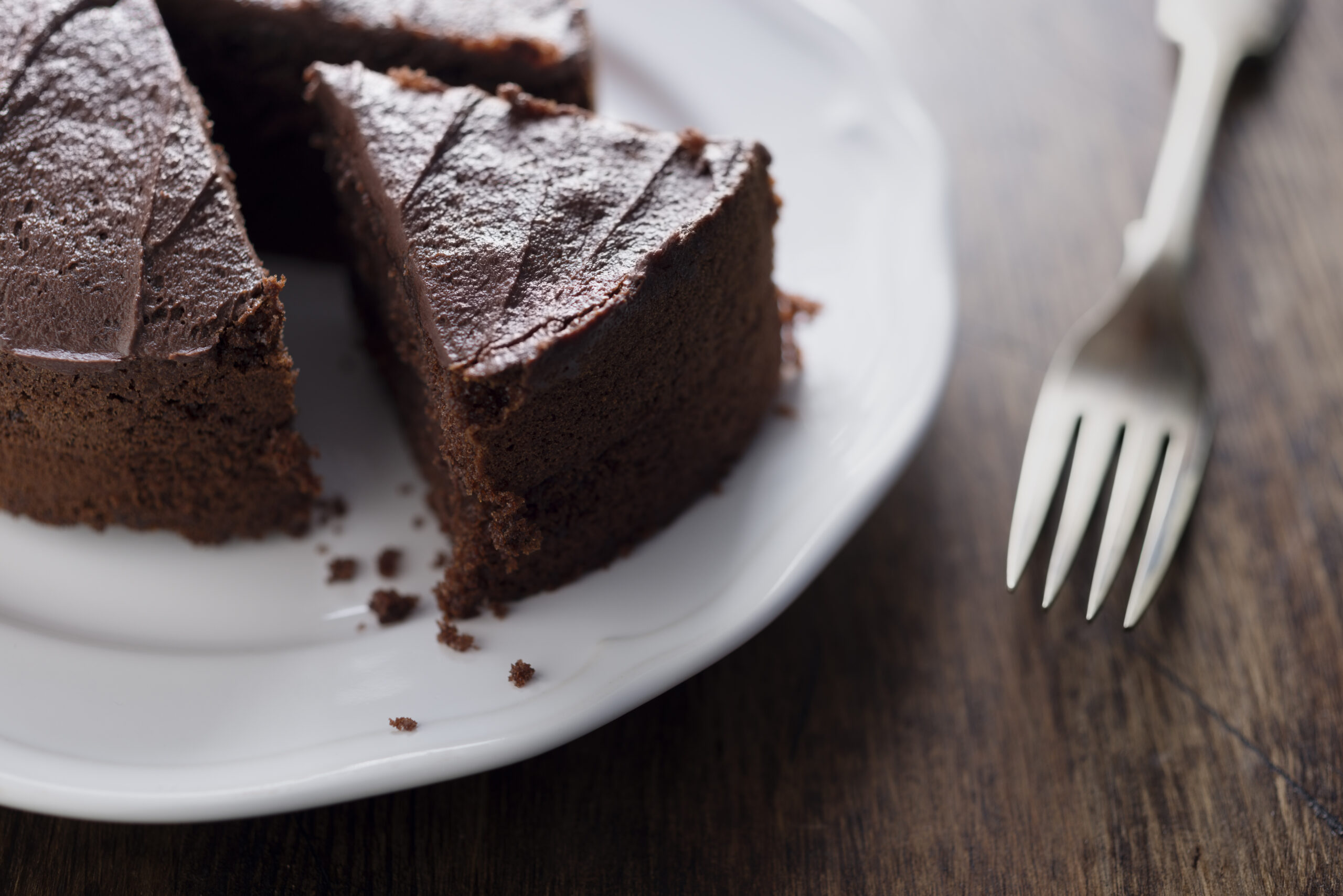 Whole backlit Chocolate Cake on a white plate, with old vintage fork and piece sliced.