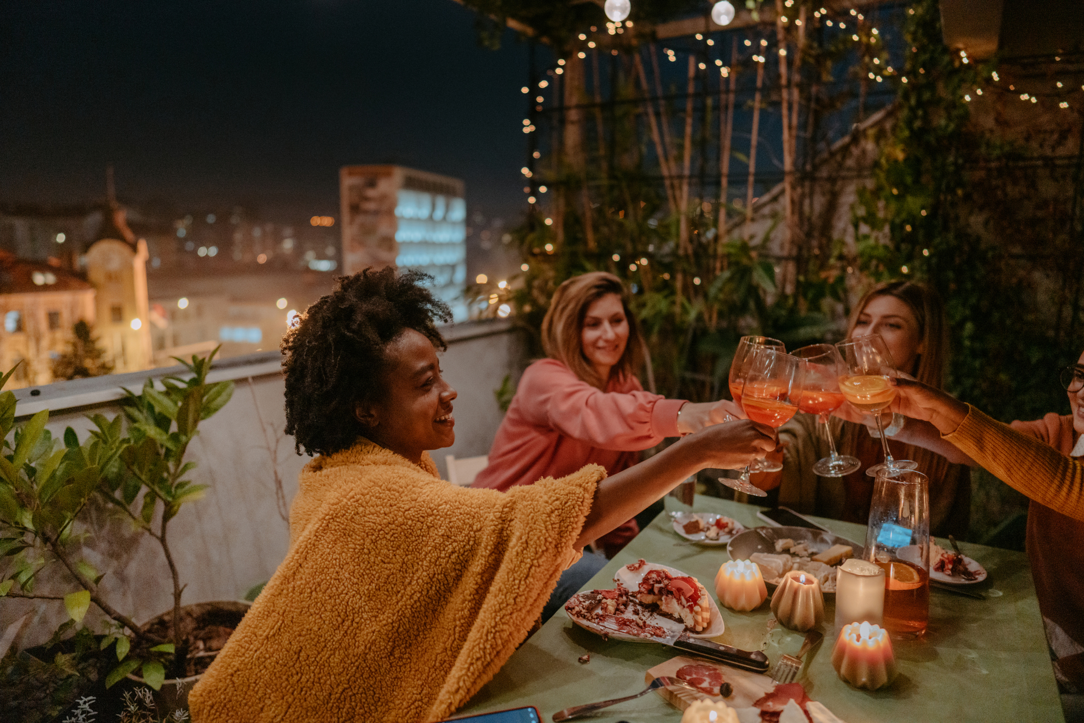 Photo of young women celebrating a birthday by drinking wine, eating cake, and enjoying each other's company while sitting on a terrace.