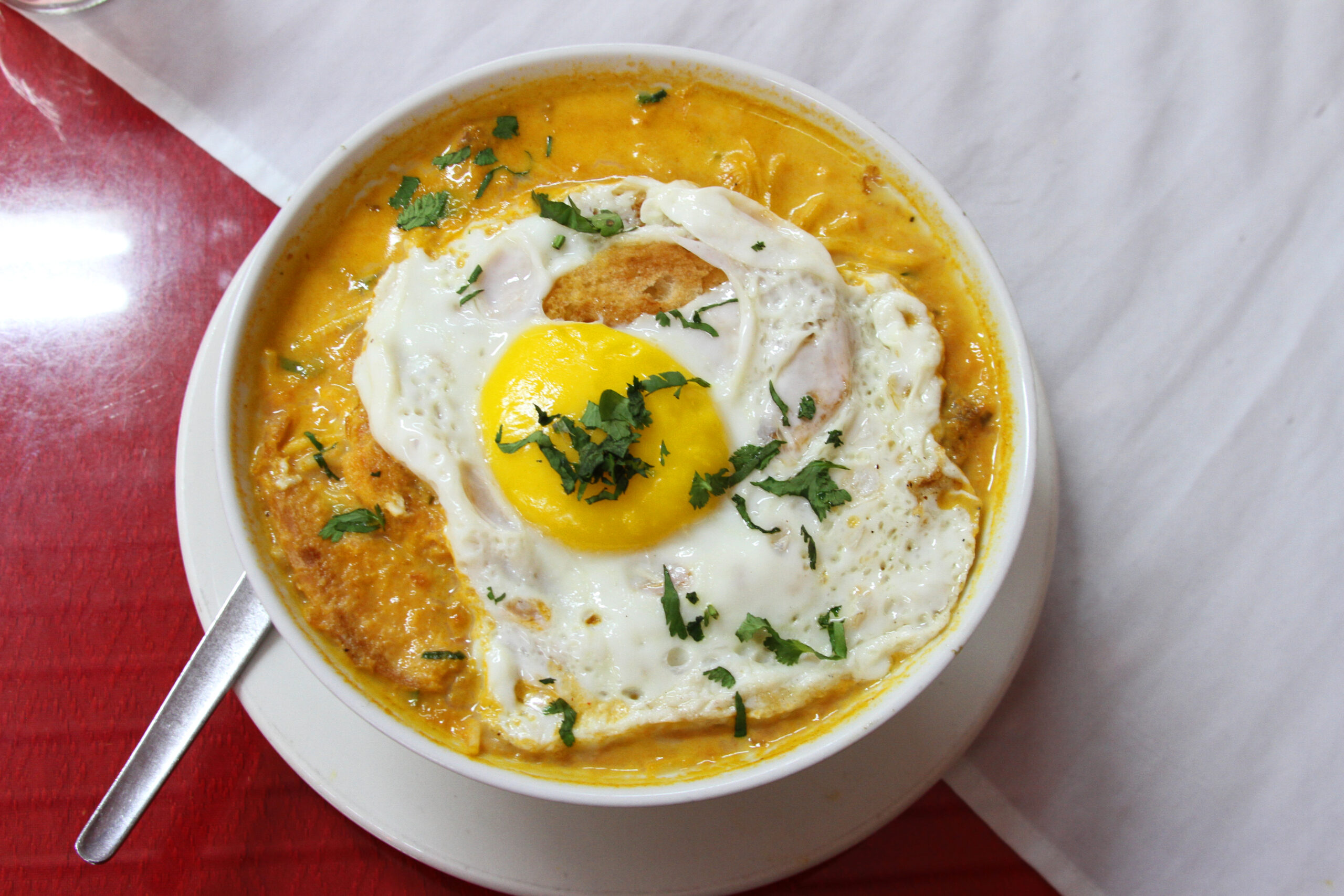 Bowl of Creole beef soup with spaghetti and a fried egg on top in Peru