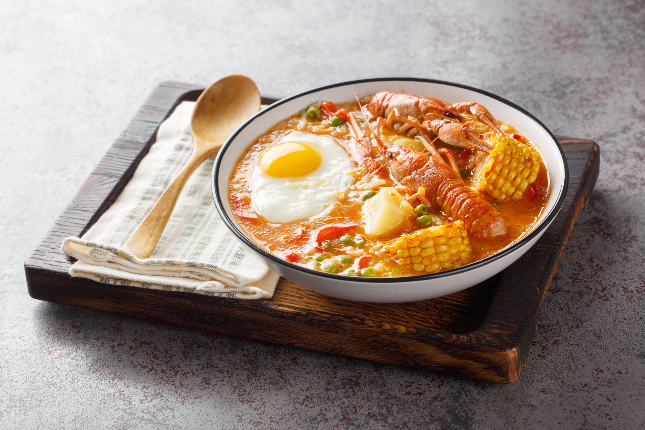 Chupe de Camarones Peruvian Crawfish Chowder with tomatoes, corn, pepper, potato, green peas and egg close-up on a bowl on the table. Horizontal