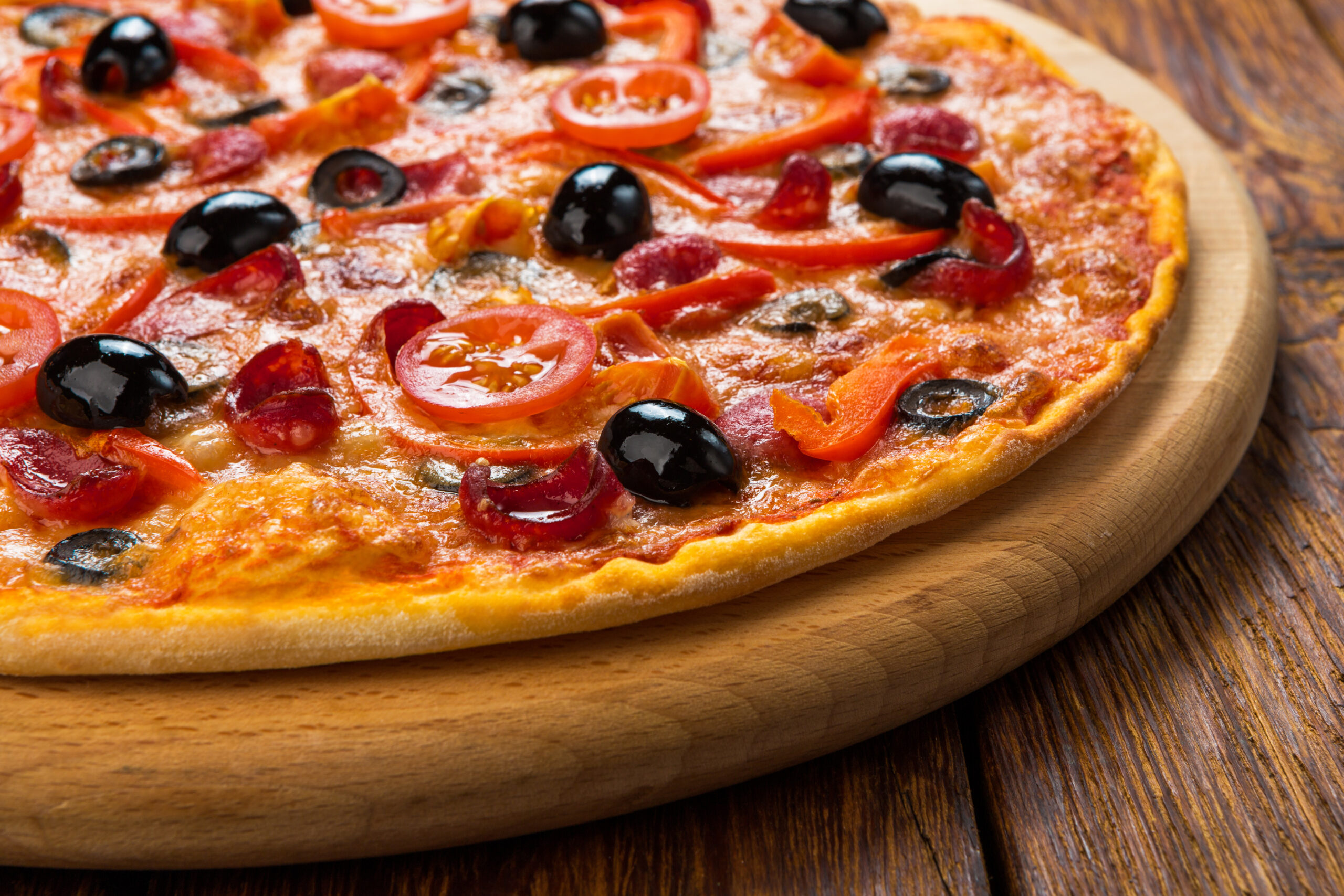 Delicious italian pizza with salami pepperoni, cherry tomatoes and black olives - thin pastry crust at wooden table background