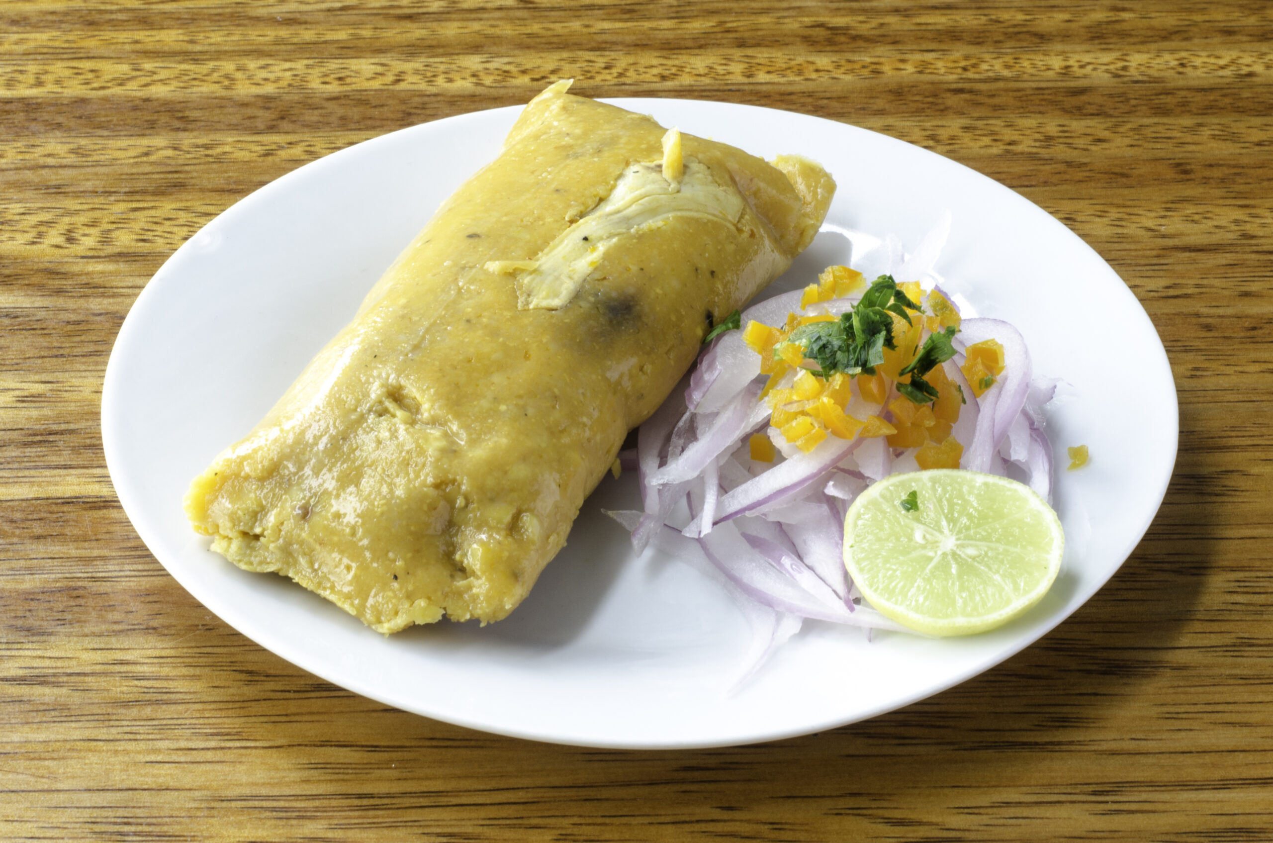 Peruvian tamale, traditionally eaten for breakfast on Sundays, made of corn and chicken and served with salsa criolla - onion salad