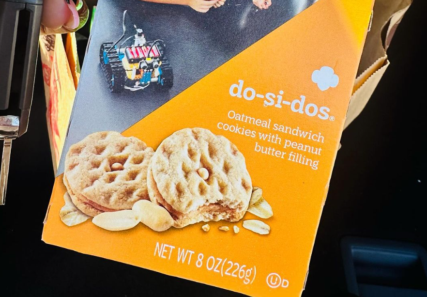 A woman's hand holding a box of Do-Si-Do Girl Scout Cookies, Instagram