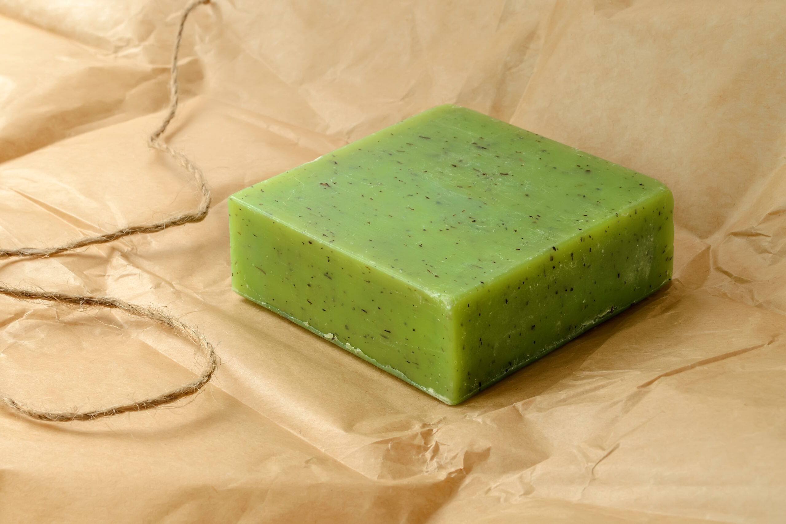 Green handmade herbal soap bar on a brown wrapping paper. Natural toiletries and hygiene products with herbs and essential oils. Front view.