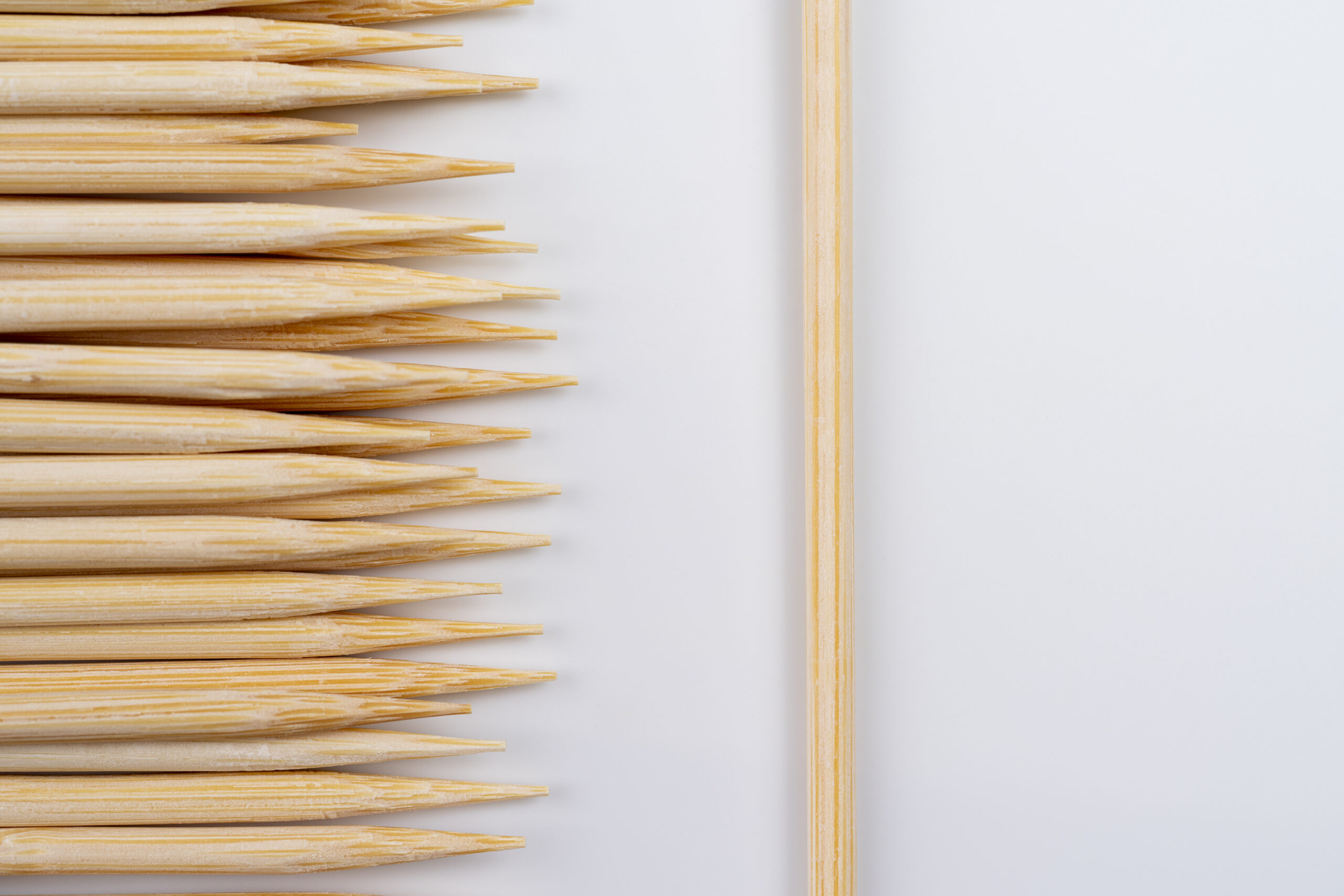 Many wooden bamboo skewers against solid white background , concept of many or one skewers on a white backdrop , wooden skewers close up