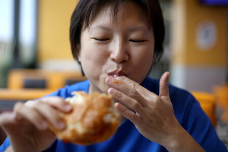 An Asian woman is enjoying deep fried chicken burger