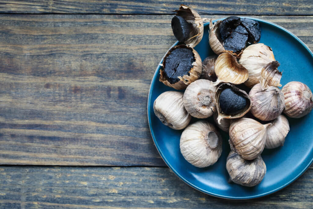 Table top view of superfood black garlic cloves on a rustic wooden table with bulbs. Selective focus with blurred background and copy space.