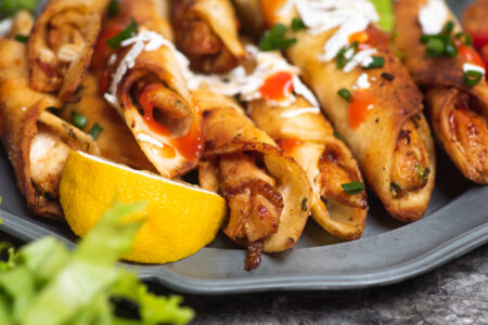 chicken small tacos called taquitos or dorados with dipping sauces and food ingredients on a plate.