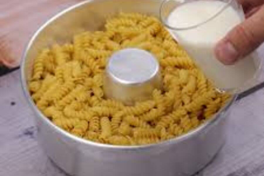 Hand pouring milk on a pasta bowl.