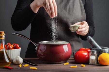 The chef preparations spaghetti and pasta, salt water, against a dark background, the concept of cooking. Woman salting water before cooking pasta fusilli.