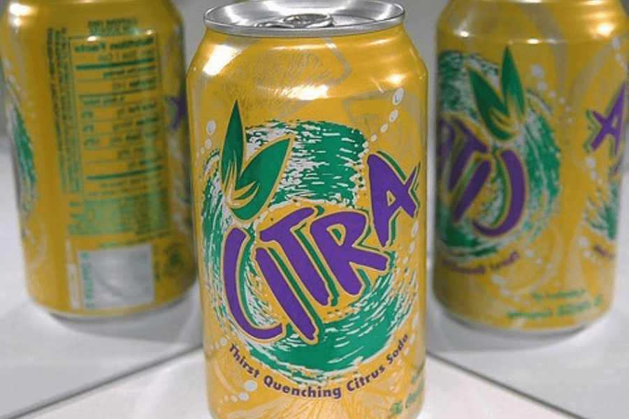 This image shows a can of Citra soda, featuring a vibrant yellow background with green and purple branding. The design includes a swirling citrus graphic and the tagline "Thirst Quenching Citrus Soda," emphasizing its refreshing nature.