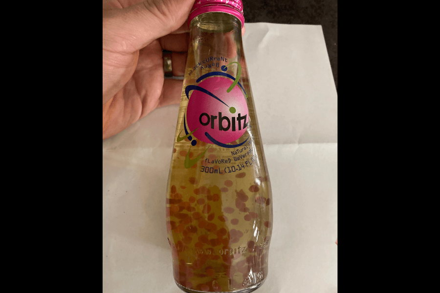 This image shows a bottle of Orbitz, a novelty beverage featuring suspended edible spheres within a clear liquid. The label highlights a "Black Currant Berry" flavor with vibrant pink and purple branding, adding a retro-futuristic touch.