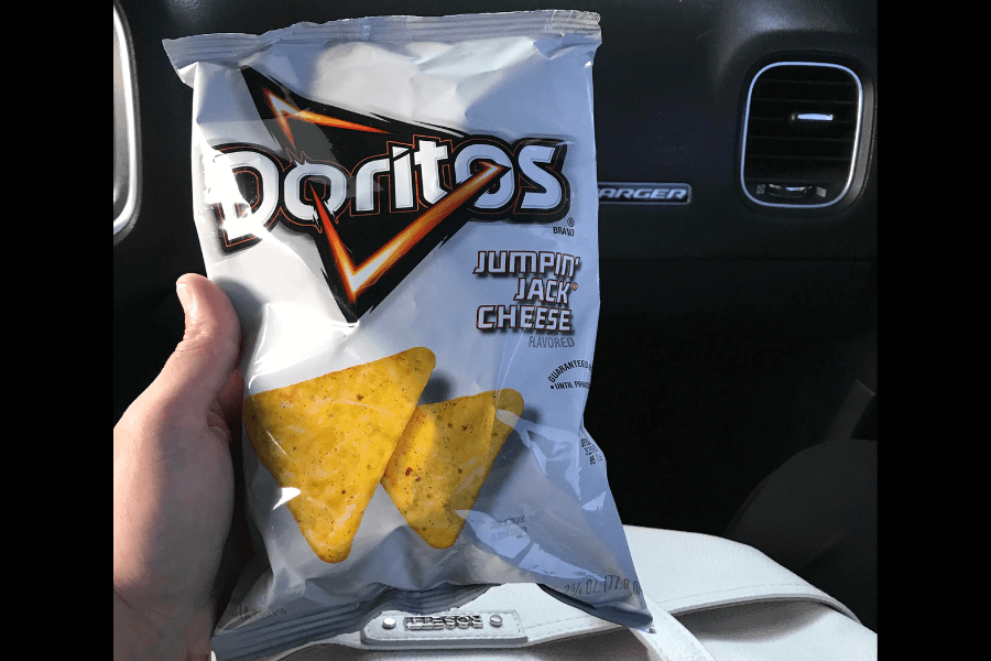 A bag of Doritos in the flavor "Jumpin' Jack Cheese," featuring a white and silver packaging design with orange and black accents. The front of the bag displays two triangular chips with visible seasoning. The bag is held by a hand inside a car, with the dashboard and air vent visible in the background.