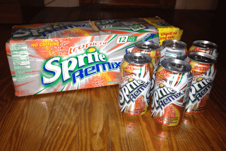 This image showcases a 12-pack of Tropical Sprite Remix soda with several cans removed and placed beside the box. The cans feature a vibrant design with orange, green, and white accents, emphasizing its tropical flavor and caffeine-free branding.