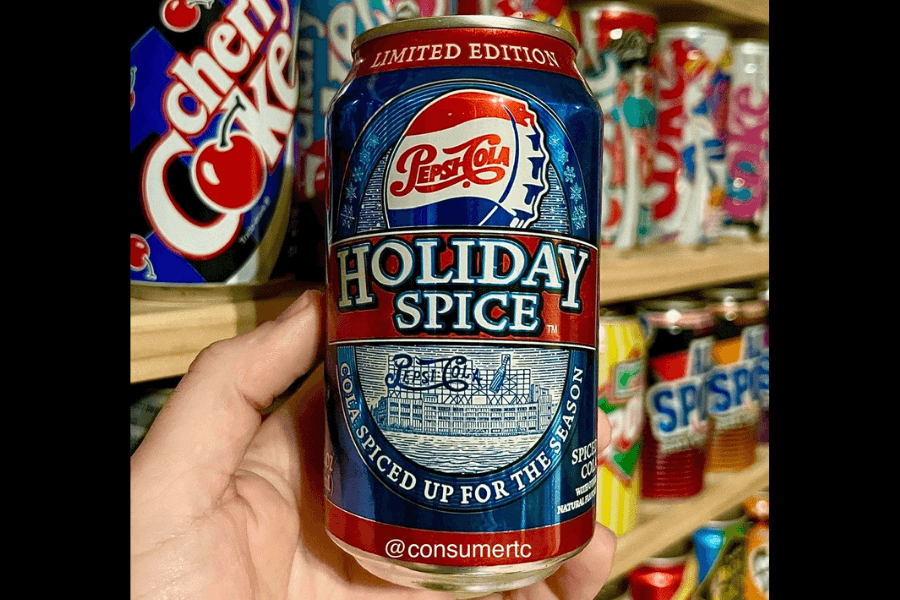 This image features a limited edition can of Pepsi Holiday Spice, showcasing a festive design with red, blue, and white accents. The label highlights the tagline "Cola spiced up for the season," with decorative illustrations evoking a holiday theme.