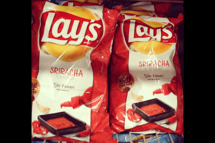 Bags of Lay's chips in the "Sriracha" flavor, featuring a red and white design. The packaging includes an image of a black dipping dish filled with sriracha sauce and red chili peppers. The flavor is credited to Tyler Raineri from Lake Zurich, IL, and the bags promote a "Vote to Save Your Fave" campaign. The bags are displayed on a store shelf.