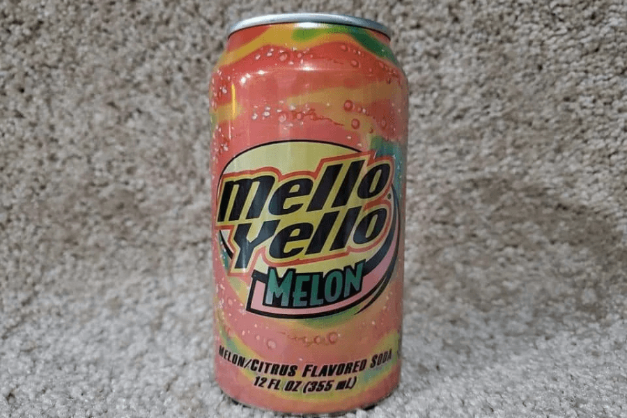 This image displays a can of Mello Yello Melon soda with a vibrant pink, yellow, and green design. The branding emphasizes its melon and citrus flavors, featuring bubbly graphics and bold black text.