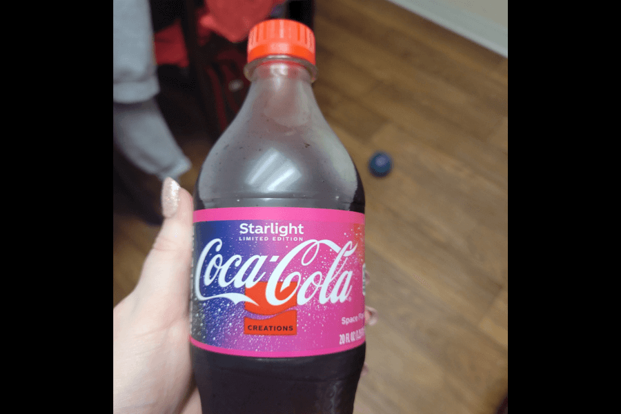 This image features a bottle of Coca-Cola Starlight, a limited edition flavor from the Coca-Cola Creations series. The label has a cosmic design with pink and purple tones, showcasing a "Space Flavored" theme, and the red cap complements the branding.