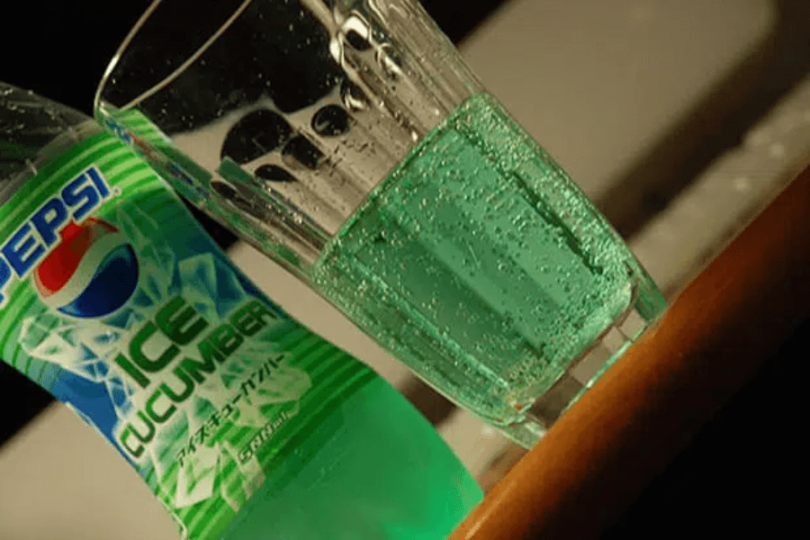 This image shows a bottle of Pepsi Ice Cucumber alongside a glass filled with the bright green soda. The bottle features a refreshing green design with ice-themed graphics, emphasizing its unique cucumber flavor.