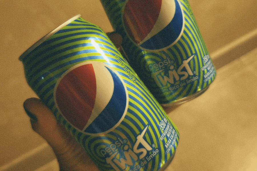 This image shows two cans of Pepsi Twist, featuring a bright and dynamic green-and-yellow striped design. The cans highlight the lime-flavored twist with bold text and the iconic Pepsi logo prominently displayed.