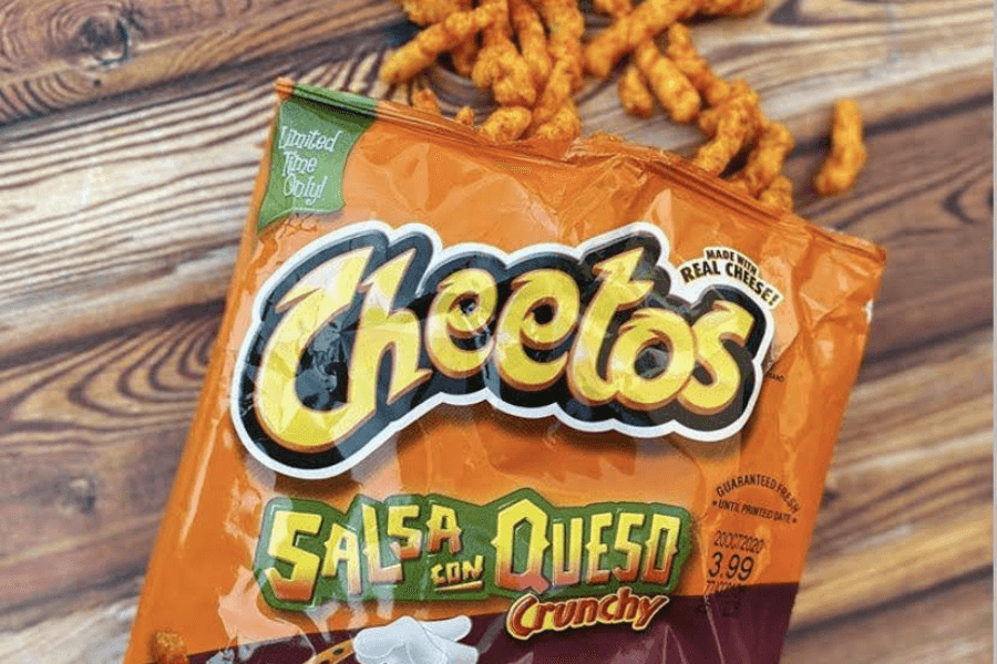 A bag of Cheetos in the "Salsa Con Queso Crunchy" flavor, featuring an orange design with a "Limited Time Only!" label. The packaging highlights bold text and an image of cheese and salsa, emphasizing the spicy and cheesy flavor. Some of the crunchy Cheetos are spilled out onto a wooden surface.