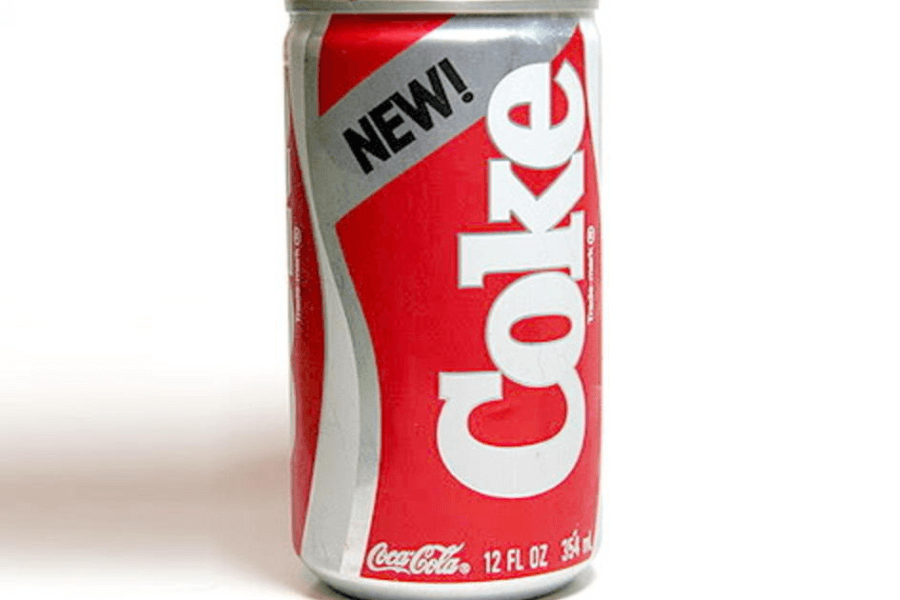 This image displays a 12-ounce can of "New Coke," featuring a red and silver design with bold white lettering. The word "NEW!" is prominently printed at the top.