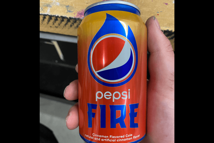 This image displays a can of Pepsi Fire, featuring a fiery red and orange design with a blue flame graphic surrounding the Pepsi logo. The label highlights its cinnamon-flavored cola, combining bold visuals with a spicy flavor theme.