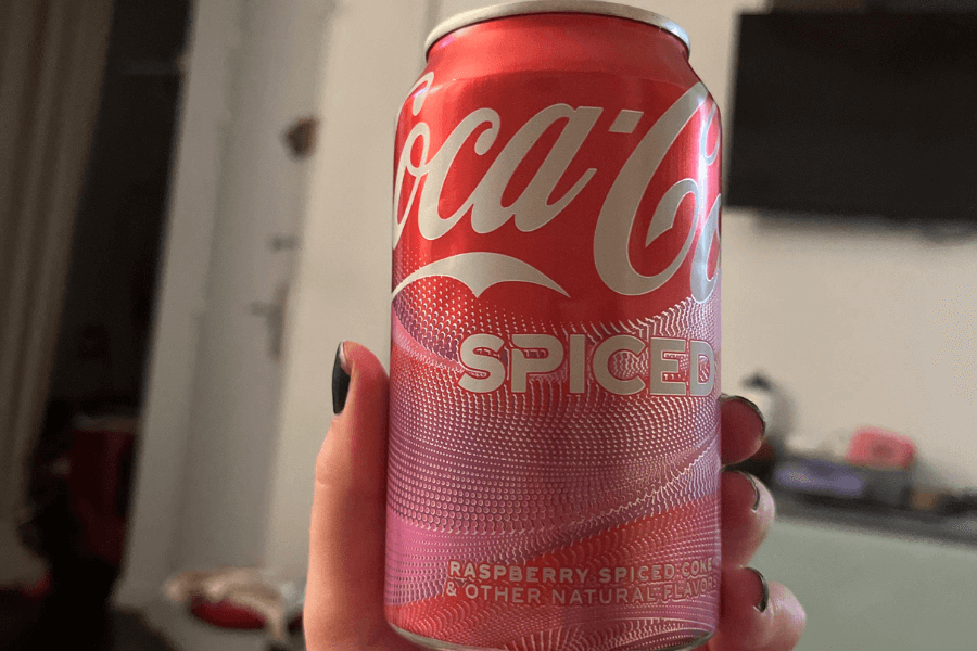 This image showcases a can of Coca-Cola Spiced, featuring a red and pink gradient design with a textured pattern. The label highlights a "Raspberry Spiced Coke" flavor, blending the iconic Coca-Cola branding with a festive and unique twist.