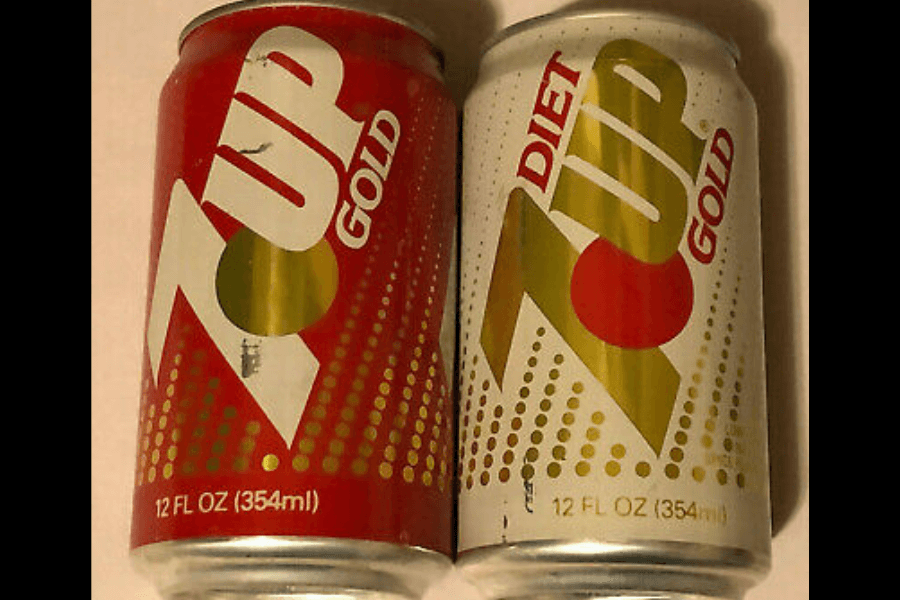 This image shows two 12-ounce cans of "7UP Gold," one regular in red and the other a "Diet" version in white. Both feature bold branding with a gold and red logo accented by dotted gradient patterns.