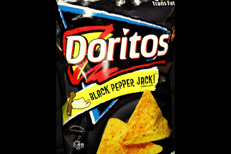 A bag of Doritos in the "Black Pepper Jack" flavor, featuring a black design with a yellow banner displaying the flavor name and an illustration of a pepper mill and cracked pepper. The packaging showcases seasoned triangular chips at the bottom and highlights "0g Trans Fat" in the corner.