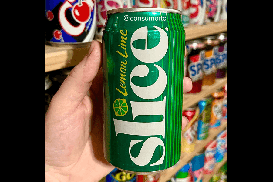 This image shows a hand holding a can of Slice Lemon Lime soda, featuring a green design with bold white text and a small lemon-lime illustration. The background includes shelves stocked with other soda cans, adding a nostalgic or collectible vibe to the scene.