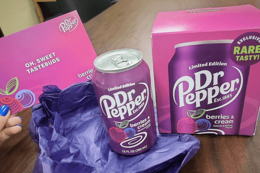 This image showcases a limited edition can of Dr Pepper Berries & Cream soda, placed next to its matching purple packaging and a card that reads, "Oh, sweet tastebuds." The vibrant purple design features berry illustrations, emphasizing the unique flavor.