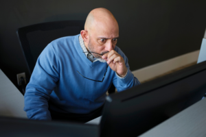 Uma aluna do quarto ano foi suspensa — o que ela disse em seguida deixou o diretor atordoado Bald man in a blue sweater looks intensely at a computer monitor, holding his glasses near his mouth in a thoughtful or concerned pose. He sits at a desk in a modern office setting.