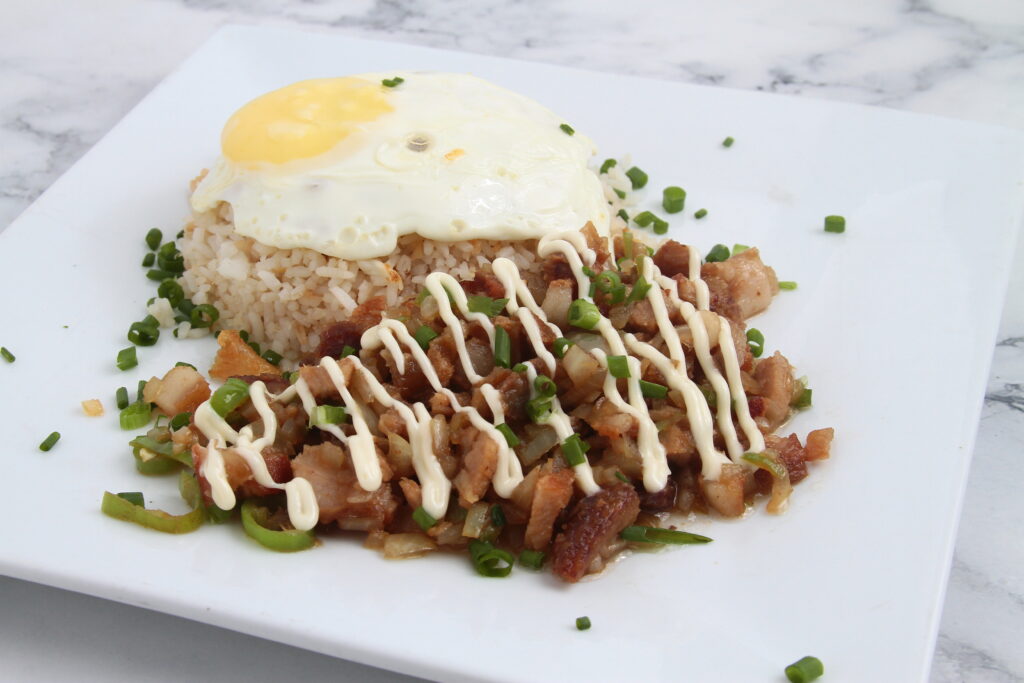 Fotografía de comida filipina recién cocinada llamada Sisig silog o piel y grasa de cara de cerdo picada, servida con huevo y arroz frito.