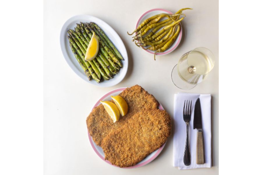 Foto tomada desde arriba de varios platos conteniendo chauchas y una milanesa recién cocinada