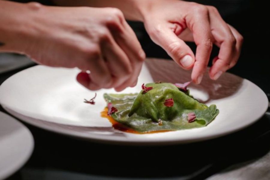 Manos acomodando un ravioló verde en un plato