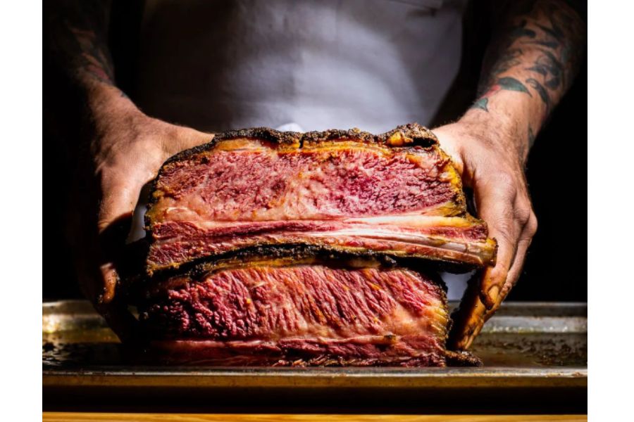 Dos manos de hombre sosteniendo un trozo grande de pastrón de novillo jugoso recién cocinado