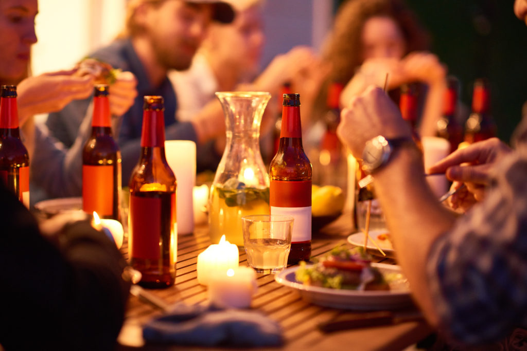 Close-up of young friends eating tasty food and drinking beer from bottles at night party