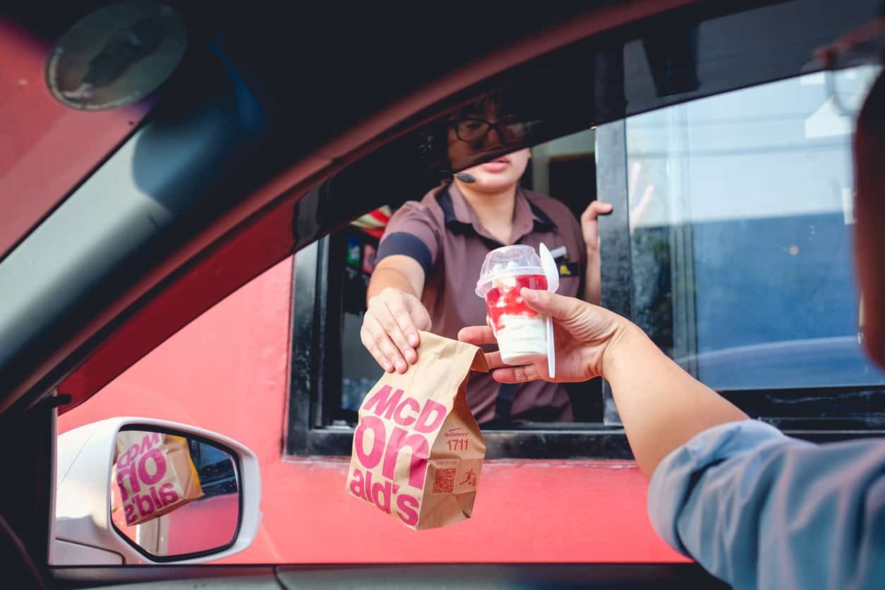 McDonald’s staff handing order to a customer at a drive-thru window.