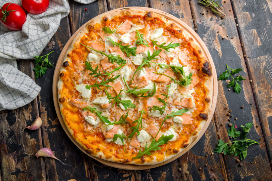 Pizza with salmon, Philadelphia cheese and aragula on old wooden table top view